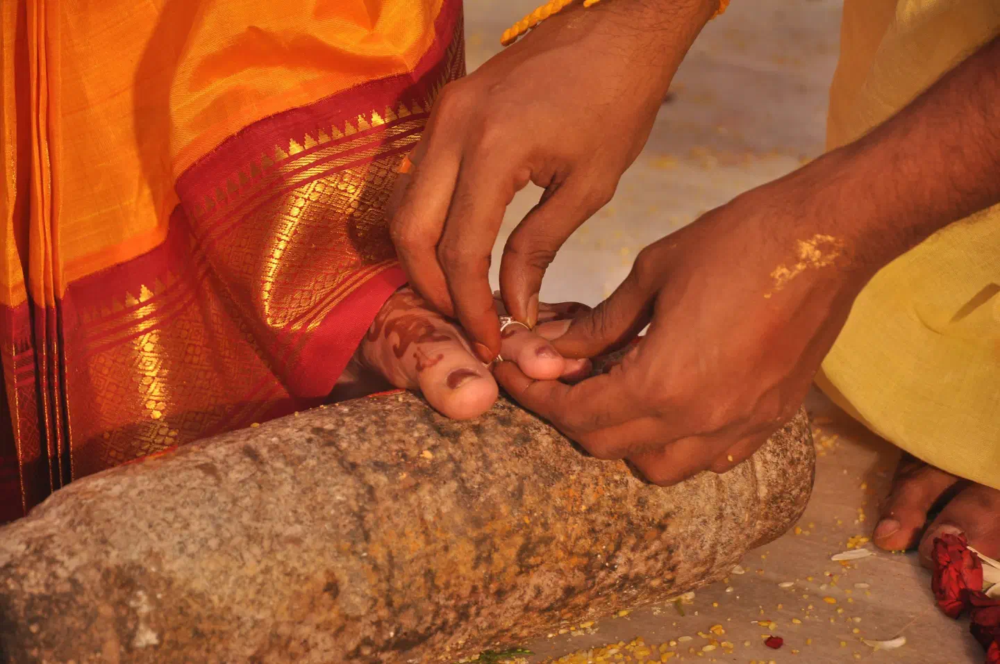 A groom placing a metti toe ring on the bride during a wedding, her foot resting on the ammi stone